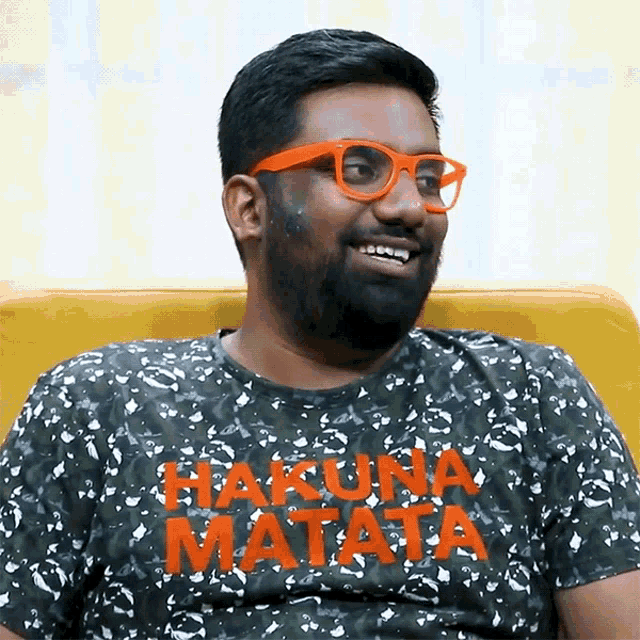 a man wearing glasses and a shirt that says hakuna matata smiles