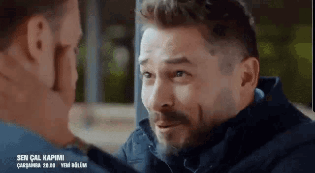 a man with a beard is looking at another man 's face in a close up .