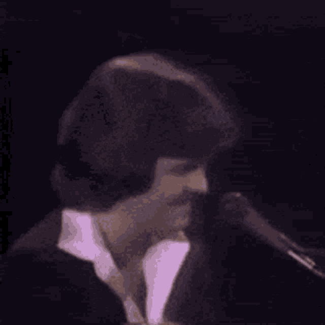 a man in a suit is singing into a microphone while sitting at a piano .