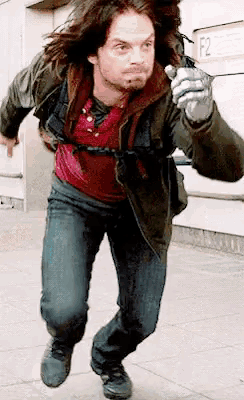 a man with long hair is running down a sidewalk while holding a sword .