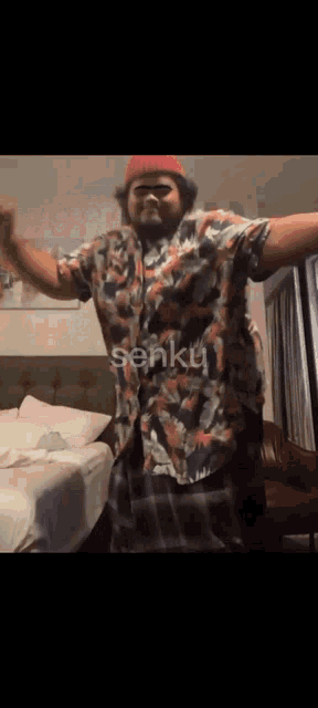 a man in a hawaiian shirt is dancing in front of a bed with the word senku written on it