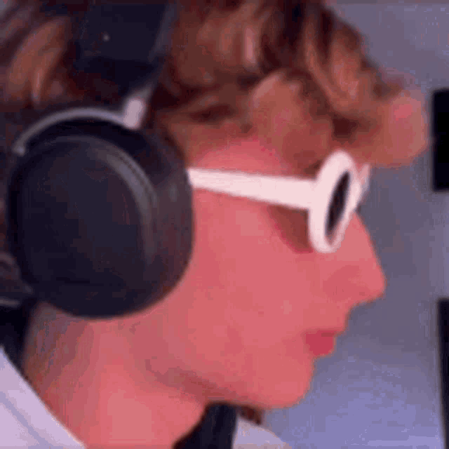 a young man wearing headphones and sunglasses is looking at the camera .