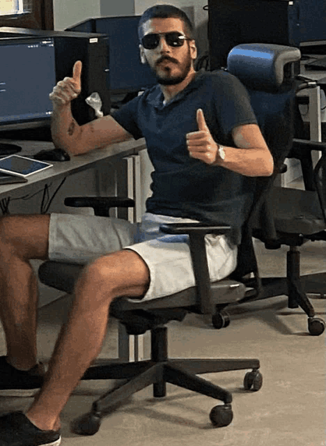 a man wearing sunglasses is sitting in an office chair and giving a thumbs up
