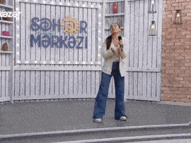 a woman is singing into a microphone in front of a sign that says sehr merkezi