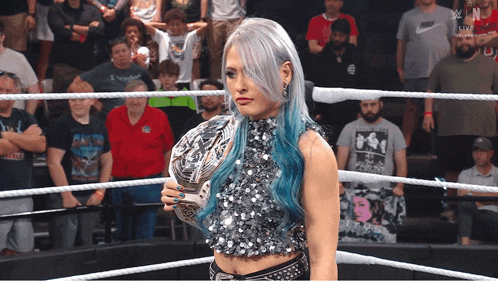 a woman holding a trophy in a wrestling ring with a crowd behind her