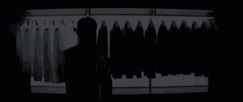 a shirtless man is standing in front of a closet filled with jackets and shirts .