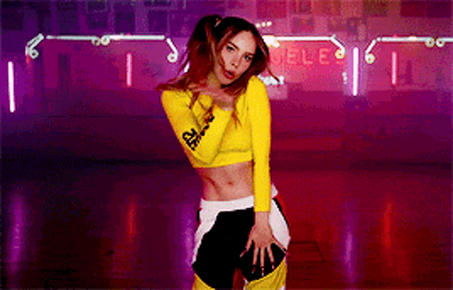 a woman in a yellow crop top is standing in front of a neon sign that says sele
