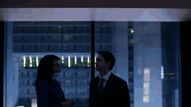 a man and a woman are standing in front of a window with a building behind them