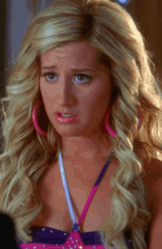 a woman with blonde hair wearing pink hoop earrings and a purple top