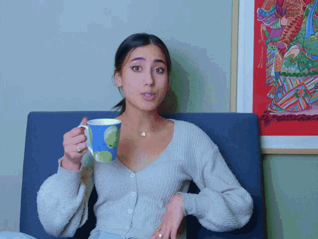 a woman sitting on a couch holding a blue mug with a green apple on it