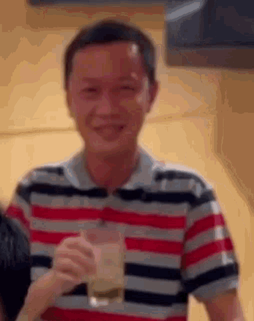 a man in a striped shirt is holding a drink and smiling .
