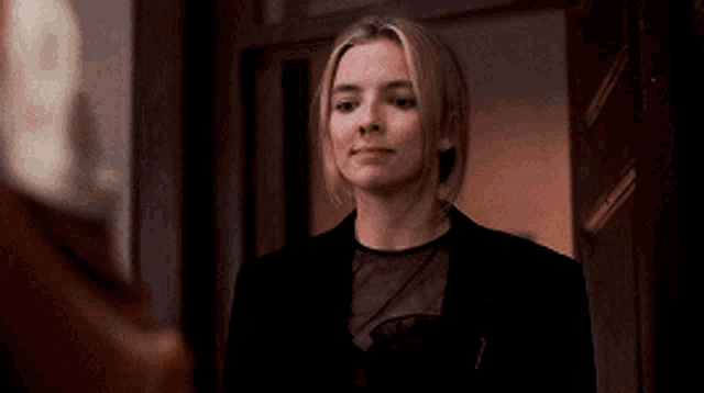 a woman in a black dress is standing in front of a door and looking at herself in the mirror .