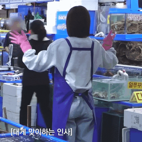 a woman wearing pink gloves and an apron stands in front of a display of seafood