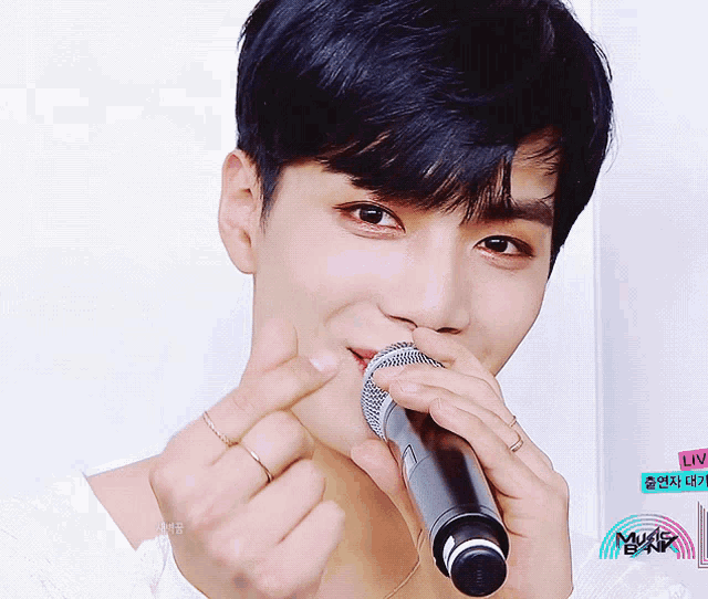 a young man is holding a microphone and making a heart with his hands