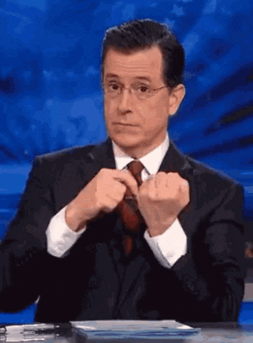 a man in a suit and tie is sitting at a desk and adjusting his tie .