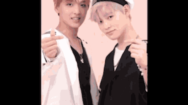 two young men with pink hair are standing next to each other and making a heart shape with their hands .