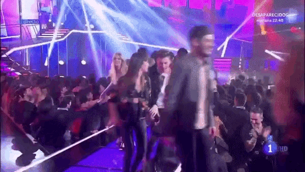 a group of people are dancing on a stage in front of a crowd with the number 1 on the screen .