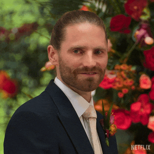 a man in a suit and tie is standing in front of flowers with a netflix logo on the bottom right
