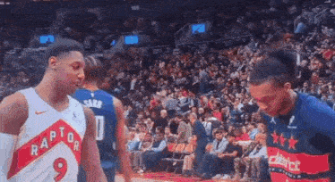 a couple of basketball players standing next to each other in front of a crowd at a basketball game .