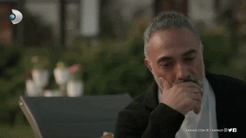 a man is sitting at a table with his hand on his mouth .