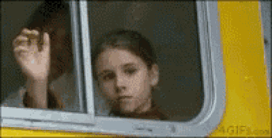 a young girl is looking out of a window of a yellow bus .