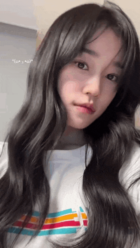 a girl with long black hair is wearing a white shirt with a rainbow stripe on it .