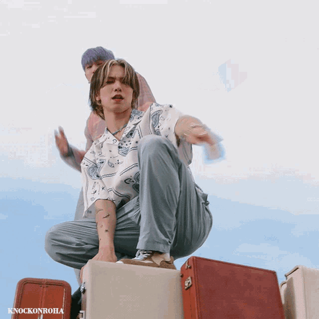 a man squatting on a suitcase next to another man with knockonroha written on the bottom