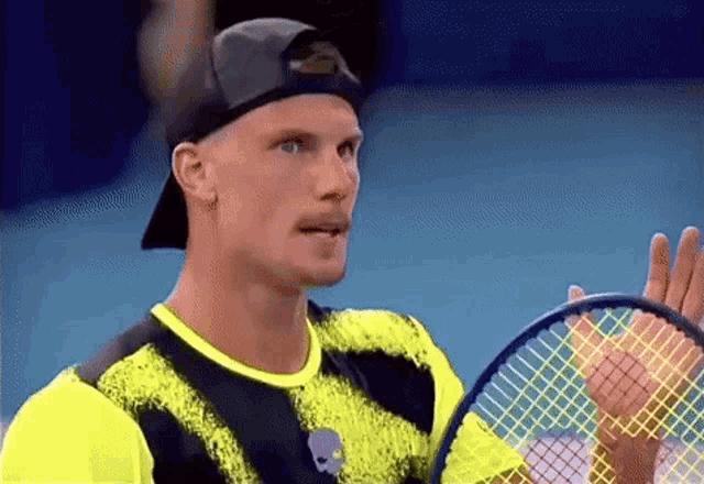a man wearing a hat is holding a tennis racquet in his hand .