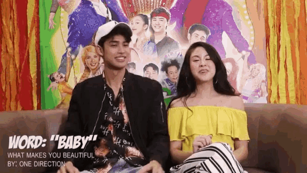 a man and woman sit on a couch in front of a poster that says word baby