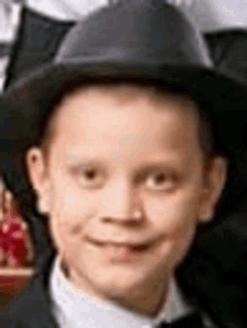 a young boy wearing a black hat and a bow tie is smiling for the camera .
