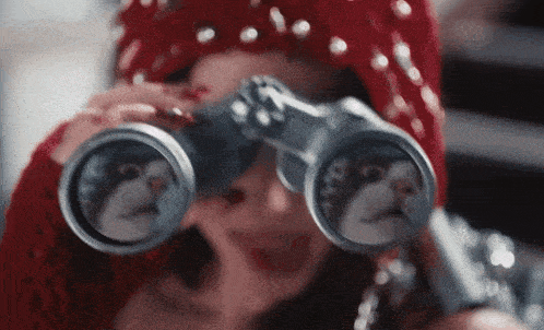 a woman is looking through binoculars with a cat on the lenses