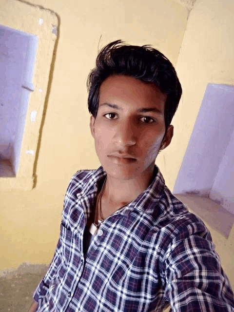 a young man in a plaid shirt takes a selfie in front of a yellow wall