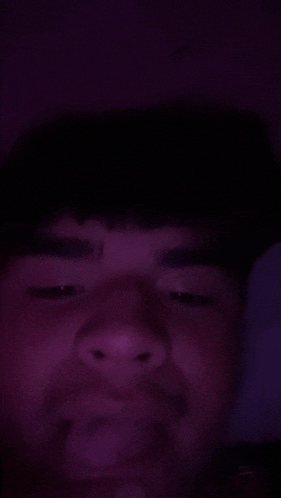 a close up of a man 's face in a dark room with a purple light behind him .