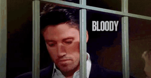 a man in a suit is behind bars in a jail cell and the word bloody is on the wall behind him .