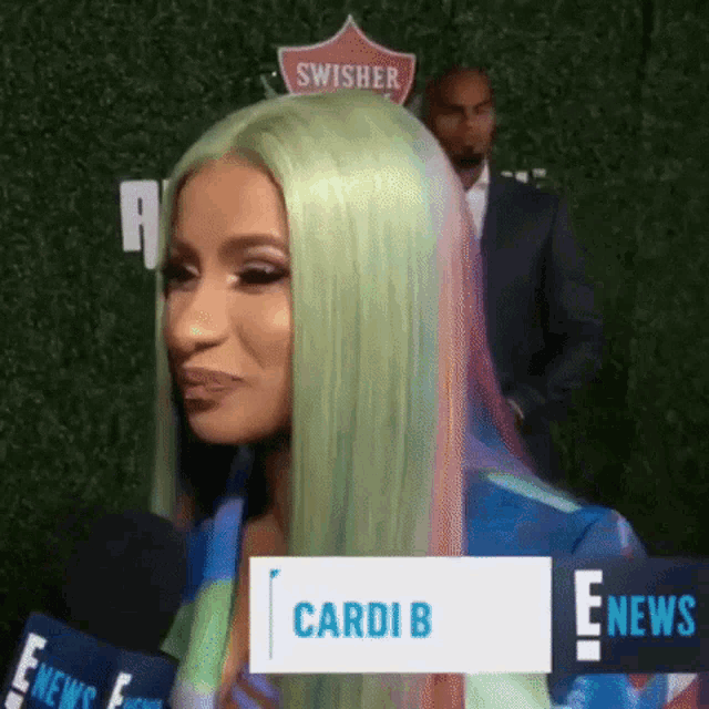 a woman with green hair is talking into a microphone in front of a sign that says swisher