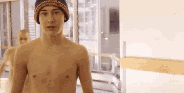 a shirtless man wearing a beanie is standing in front of a window in a room .