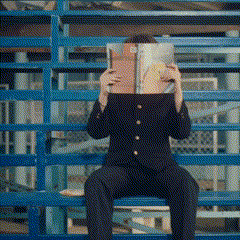 a man in a suit is sitting on a bench reading a magazine