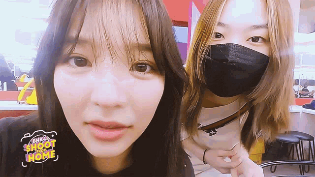 two girls wearing masks are standing next to each other in front of a sign that says bkk shoot home