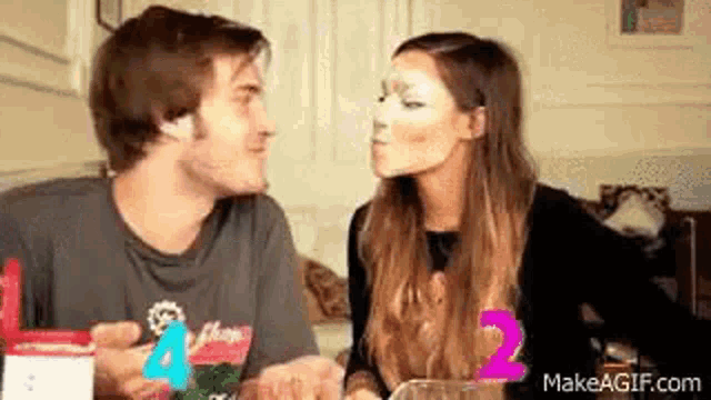 a man and a woman are kissing while sitting at a table . the woman is wearing a mask on her face .