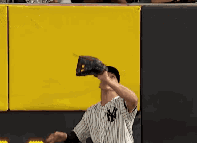 a man wearing a ny yankees jersey catches a baseball