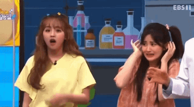 two girls are standing next to each other and one is covering her ears
