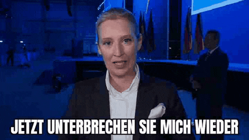 a woman in a suit and white shirt is standing in front of a blue background and talking .