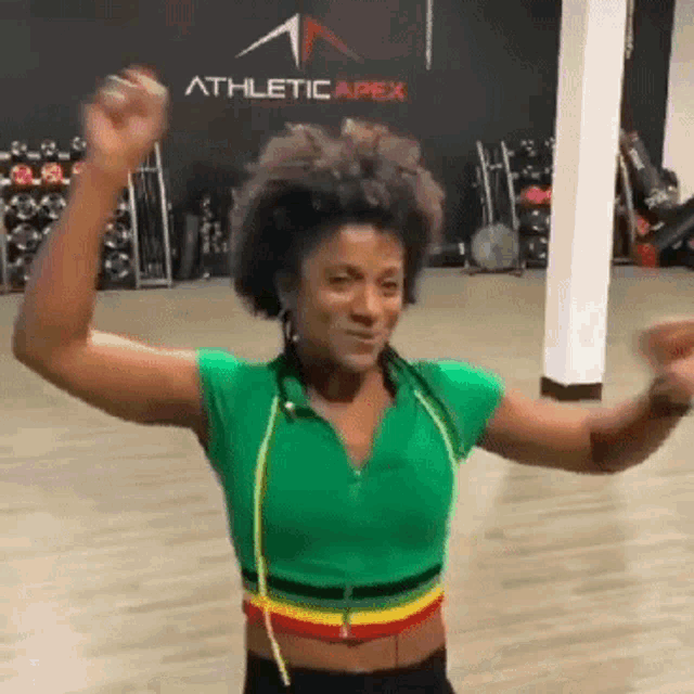 a woman is dancing in a gym with athletic apex on the wall behind her