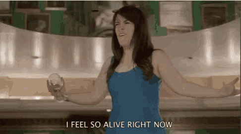 a woman in a blue dress is holding a glass of wine and says i feel so alive right now