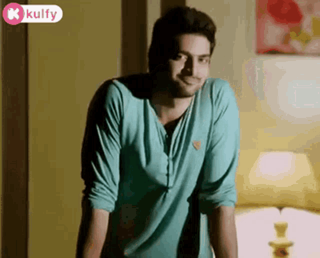 a man in a blue shirt is standing in front of a lamp and smiling .