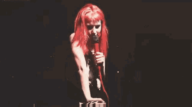 a woman with red hair is standing in front of a microphone on a stage .