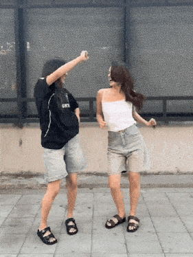 two women are dancing in front of a fence with one wearing a black shirt that says gmtn