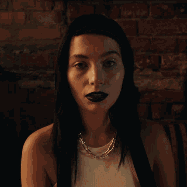 a woman with black lipstick and a silver necklace looks up at the sky