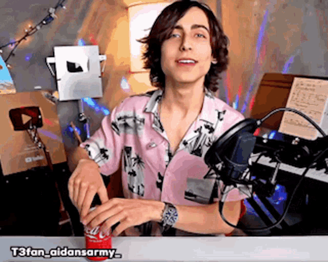 a man in a pink shirt is opening a coca cola can in front of a microphone
