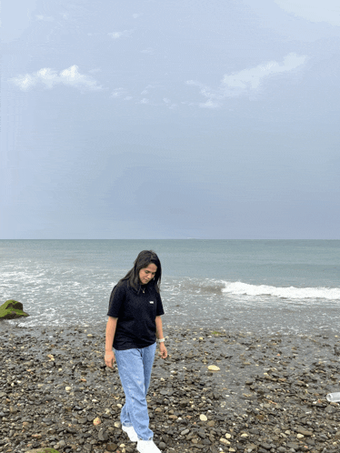 a woman standing on a rocky beach with the ocean behind her
